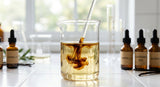 A macro photograph focusing on a glass beaker containing a rich, dark brown, viscous vanilla oleoresin being stirred into a clear, light golden carrier oil, illuminated by natural light in a laboratory setting. Shallow depth of field.