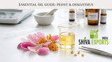 A macro photograph of pink peony petals and orange osmanthus flowers resting on a clean, white laboratory workbench next to a small glass beaker filled with clear golden oil