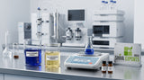 A clean, modern laboratory bench with glass beakers containing deep blue and pale yellow botanical extracts, a digital scale, and professional chromatography equipment in the soft-focus background