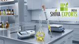Clean, modern laboratory workspace with a stainless steel surface holding a digital refractometer, a volumetric flask, and a professional glass pipette with clear yellow lemon essential oil, bright cool-toned laboratory lighting