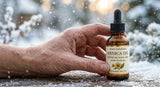 Close-up macro shot of dry, cracked skin on a hand in winter, with snowflakes subtly visible in the background, next to a bottle of Arnica Oil.