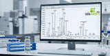 A close-up scientific laboratory shot of a GC-MS chromatogram screen displaying sharp peaks, with a transparent glass vial of clear essential oil in a laboratory rack in the soft-focused background, clean clinical lighting