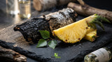 A macro photograph of charred birch bark resting next to a freshly sliced, juicy pineapple on a dark slate surface, dramatic side lighting, fine dining aesthetic, shallow depth of field