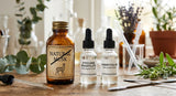 A sophisticated close-up photograph in a perfumery lab setting, showing a vintage glass perfumer's bottle labeled 'NATURAL MUSK' (crossed out) next to modern, clear glass vials labeled 'ETHYLENE BRASSYLATE' and 'AMBRETTOLIDE'. A small, stylized musk deer icon is subtly integrated into the crossed-out label. The background features blurred lab equipment and green botanical elements, symbolizing the shift from animal to sustainable sources. Soft, natural lighting.